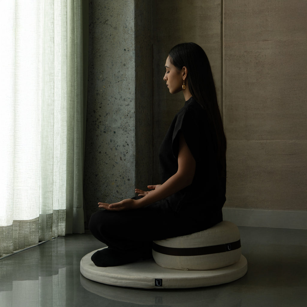 Woman sitting on a meditation cushion in a dimly lit room.